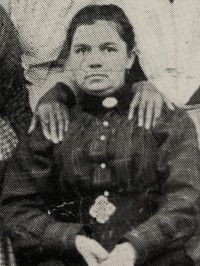 Close-up of a seated African American wearing late 19th century attire with the hands of people standing behind resting on her shoulders.
