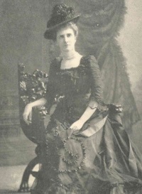 Studio photograph of a seated white woman wearing late 19th century hat and dress.