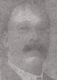 Faded headshot of an African American man with a mustache wearing glasses and early 20th century attire.