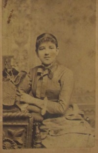 Studio photograph of a young white woman wearing late 19th century attire.