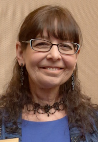 Headshot of a Monacan woman wearing glasses, beaded necklace and earrings, and a blue dress.
