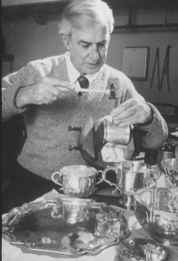 A white man working on a silver tea service.