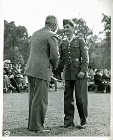 A white man in a World War 2 US Army uniform shaking hands with a man facing away from the camera.