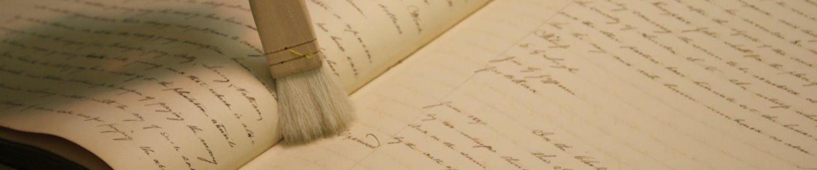conservation brush 1880x375 Bound volume laying open with shot soft bristled conservation brush held atop the the right page