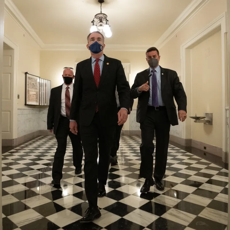 Three men walking down a hallway, toward the photographer. The men are wearing masks during the COVID-19 panemic. The man in front is Ralph Northam, Governor of Virginia at the time.