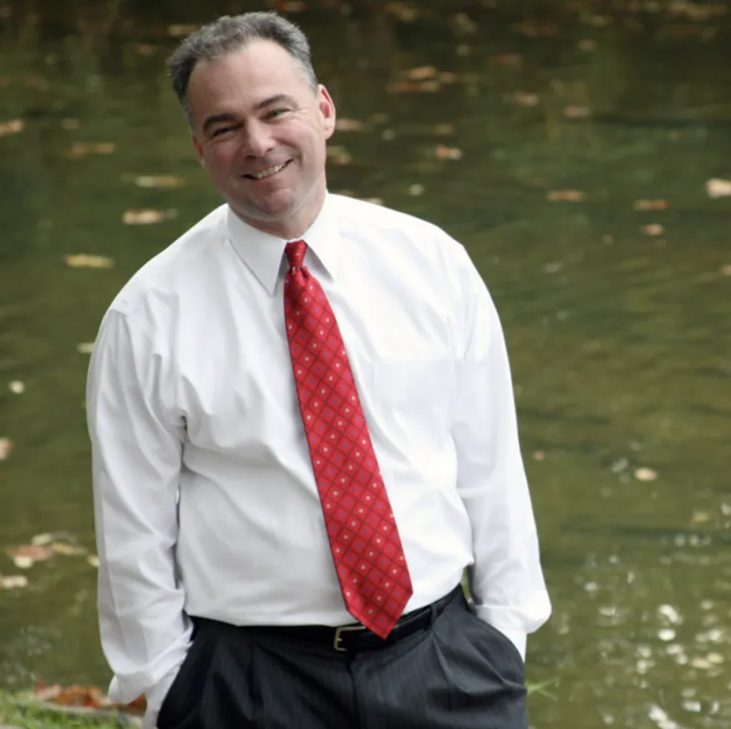 Photograph of Virginia Governor Tim Kaine from 2010. He is standing outside, and he is wearing a white dress shirt with a red tie. His hands are in his pockets, and he is smiling.