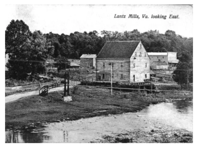 black and white photograph of wood frame buildings along a narrow road with water in the foreground