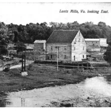 black and white postcard image of frame buildings along a road with water in the foreground